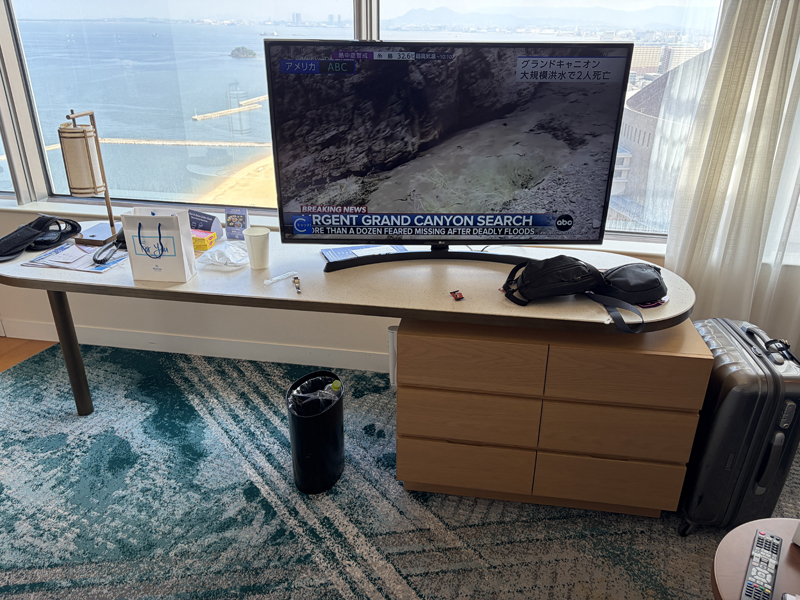 ホテルの客室のテレビが付いている。テレビの向こうには大きな窓が広がっておりPayPayドームや博多湾が見える