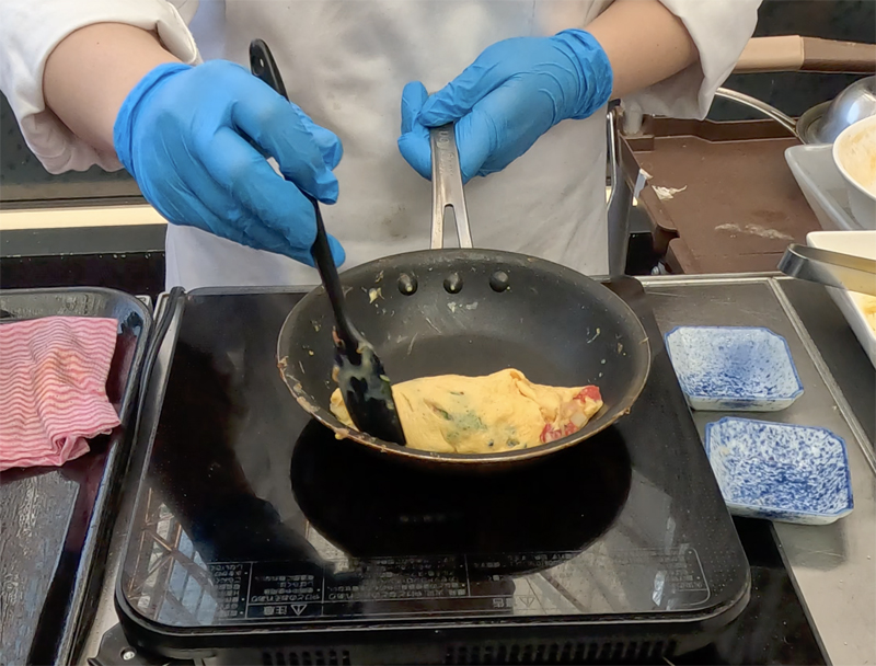 オムレツステーションのスタッフがフライパンでオムレツを焼いているところ