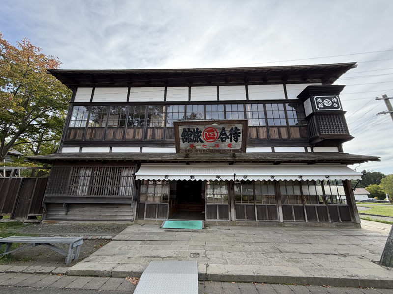 旧来正旅館（旧待合旅館）の外観。木造2階建ての和風建築で、正面に右書きで「待合旅館」と書かれた木製看板と白いサンシェードが掲げられている様子